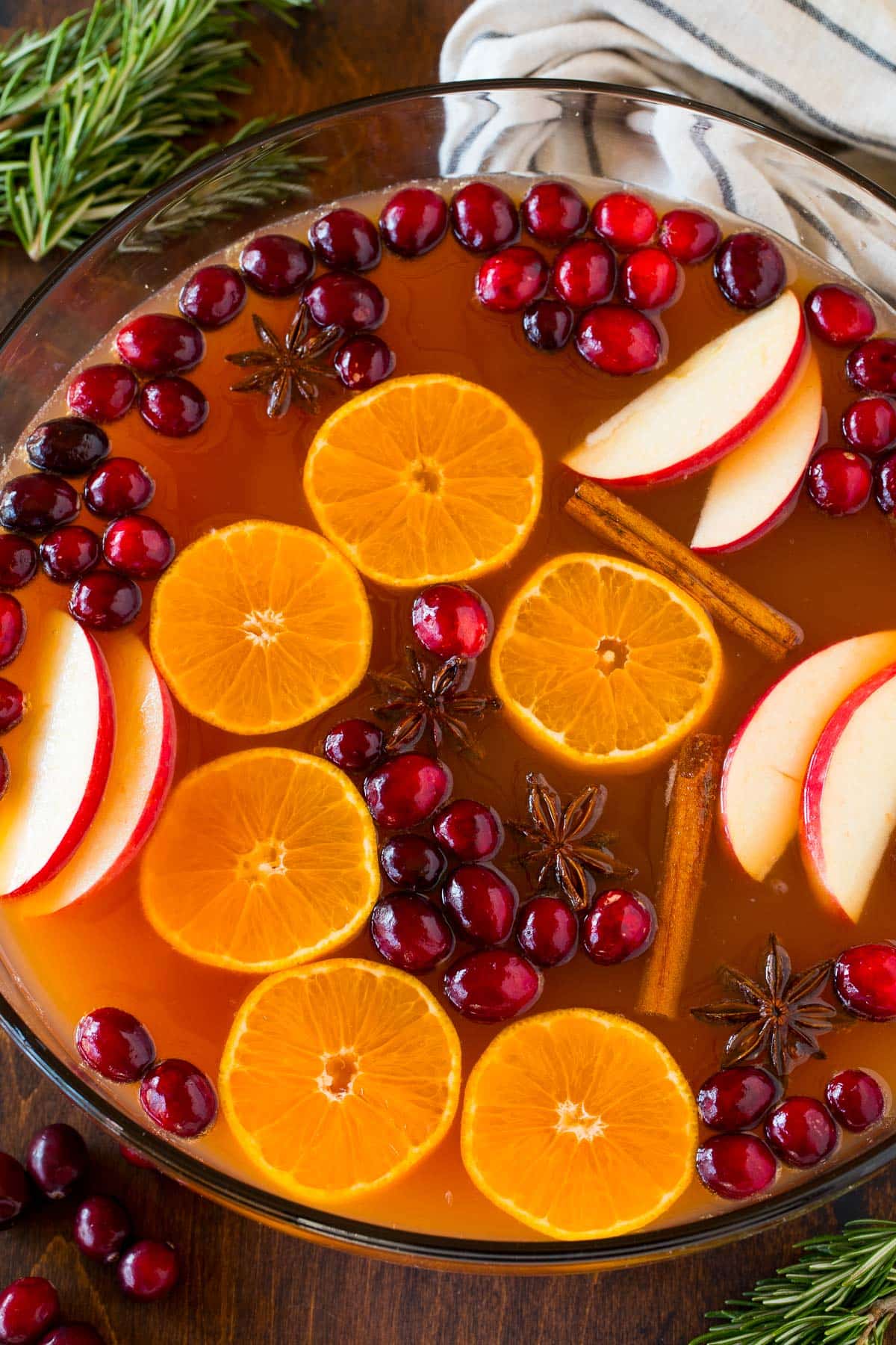 Thanksgiving punch in a large glass bowl, topped with apples, oranges and cranberries.