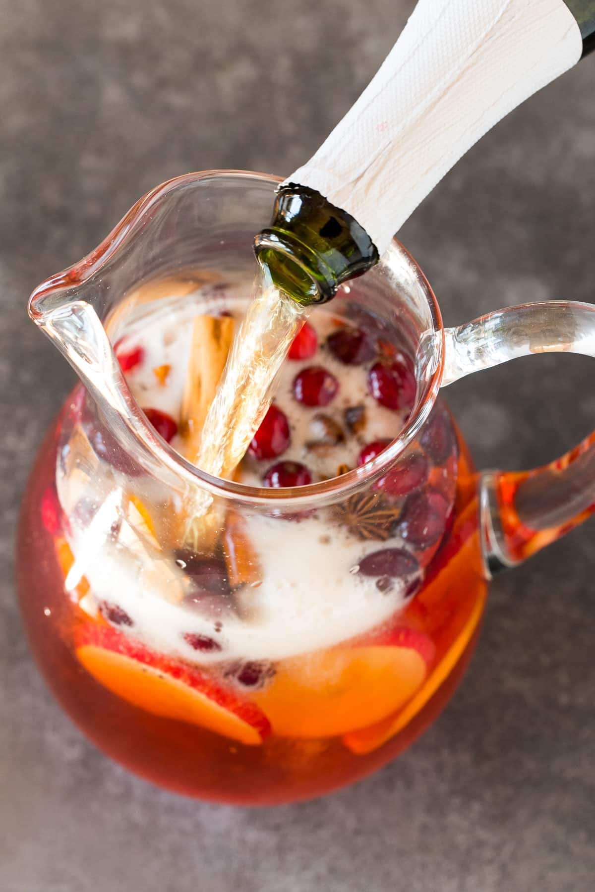Sparkling cider being poured into a pitcher of sangria.
