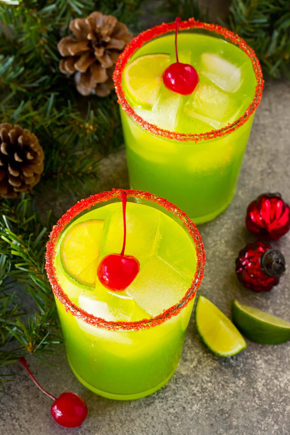 Grinch cocktail in a serving glass with a red sugar rim and maraschino cherry on top.