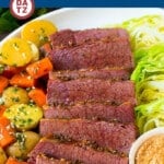 A plate with corned beef and cabbage with potatoes carrots and a little mustard.
