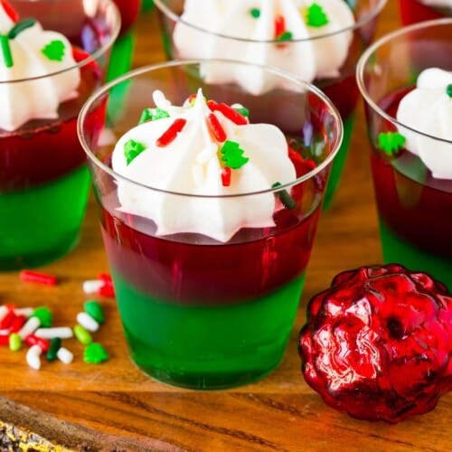 Christmas Jello shots topped with whipped cream and holiday sprinkles.