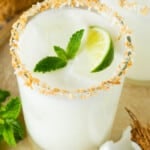 A glass of coconut margarita with a toasted coconut rim and a garnish of mint.
