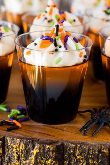 Orange and black layered Halloween Jello shots topped with whipped cream and sprinkles.