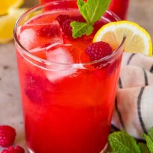 A glass of raspberry lemonade garnished with berries and a lemon slice.