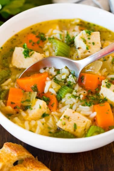 A bowl of turkey and rice soup with a spoon in it.