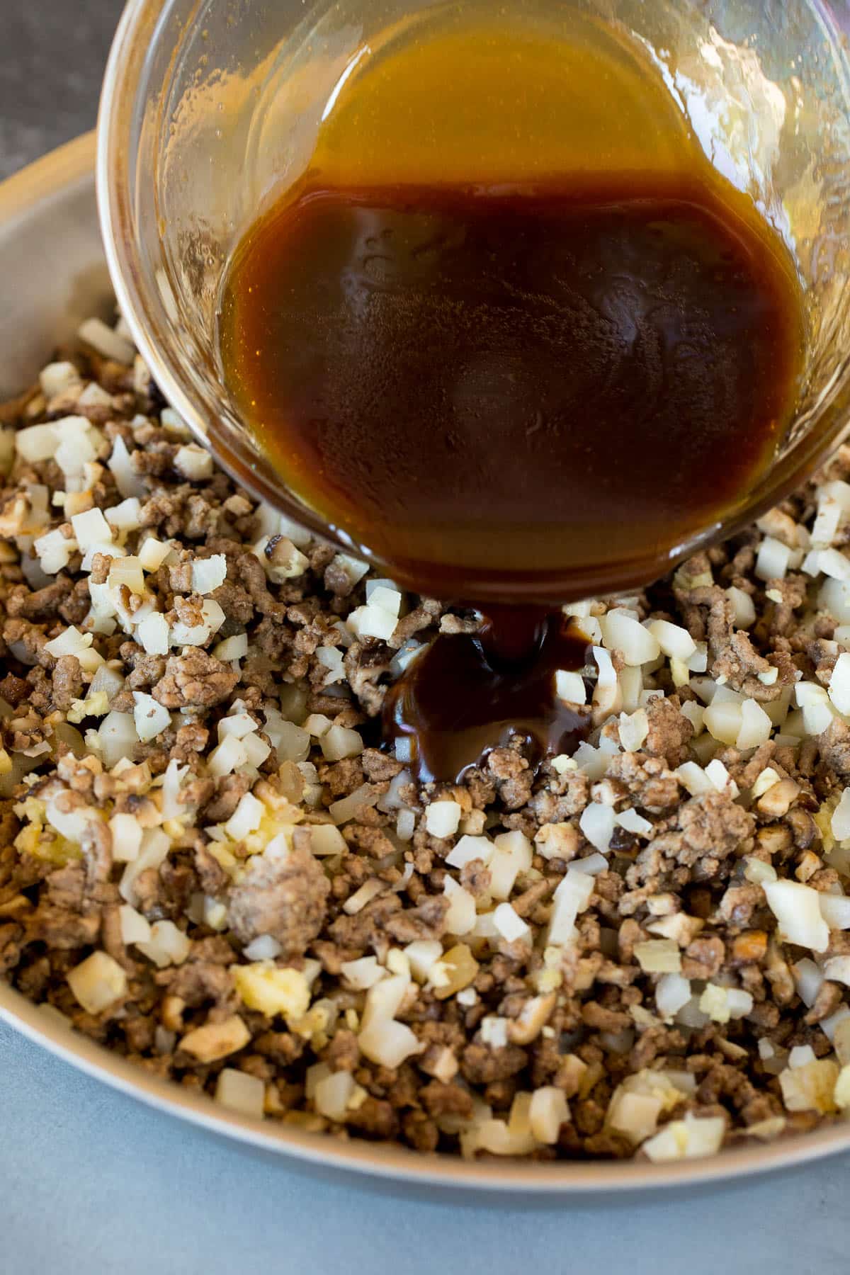 Sauce being poured into a pan of ground beef and veggies.