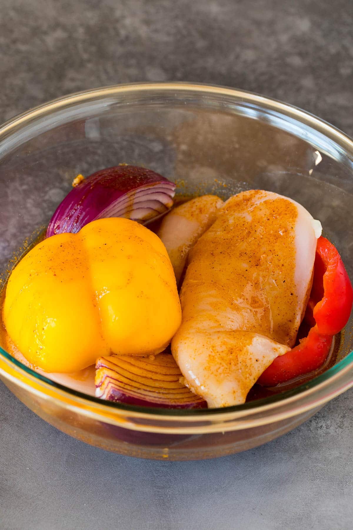 Chicken, peppers and onions in a bowl of marinade.