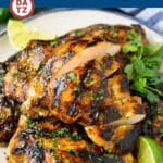 A plate of grilled chicken thighs garnished with cilantro leaves and lime wedges.