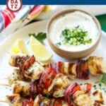 A plate of Greek chicken kabobs with a small bowl of cucumber yogurt dip.