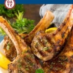 A plate of grilled lamb chops garnished with lemon wedges and herbs.