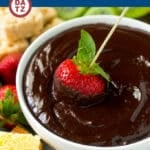A bowl of chocolate fondue with a strawberry being dipped into it.