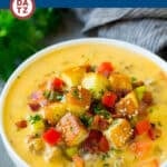 A bowl of creamy cheeseburger soup with toppings like bun croutons, diced tomatoes and diced pickles.