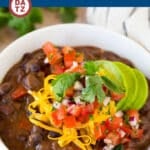 A bowl of black bean soup topped with avocado, diced tomatoes and shredded cheddar cheese.