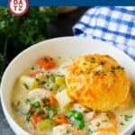 A bowl of chicken pot pie soup with a cheddar biscuit on top.