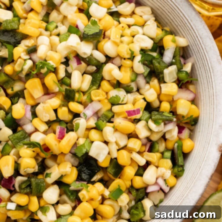 Overhead view of a white bowl of roasted chili corn salsa on a table.
