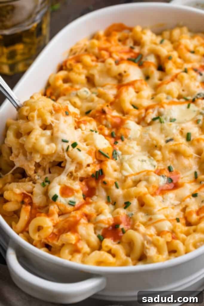 Angled view of a spoonful of buffalo chicken mac and cheese resting on a casserole dish of mac and cheese, highlighting the creamy texture and buffalo chicken pieces.