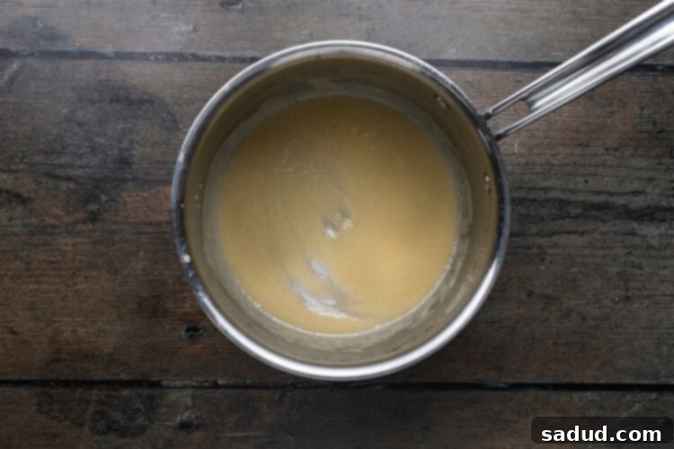 Overhead view of a silver pot of melted butter on a dark wooden background.