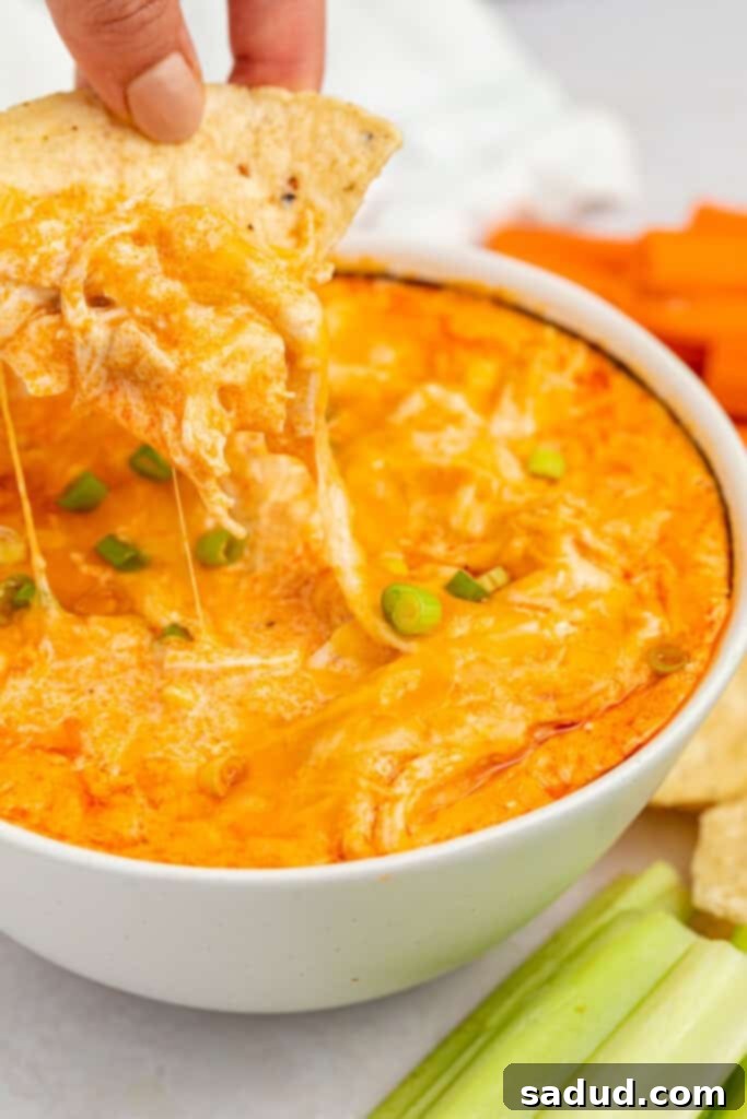 A chip being dipped into a luscious bowl of Instant Pot buffalo chicken dip, garnished with fresh green onions.