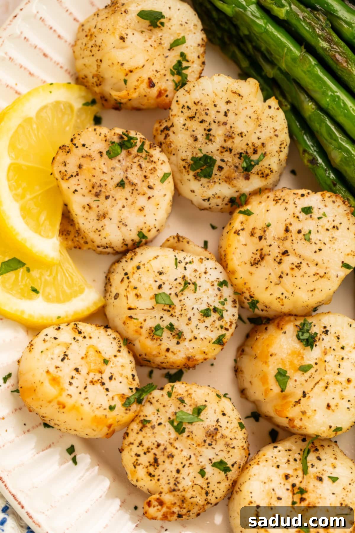 Plate of perfectly seasoned air fryer scallops with vibrant asparagus and fresh lemon slices on the side, ready to be served.