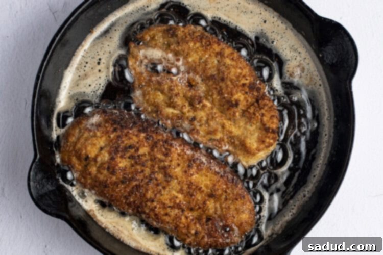 Pan-fried breaded chicken cutlets in skillet, ready for the oven.