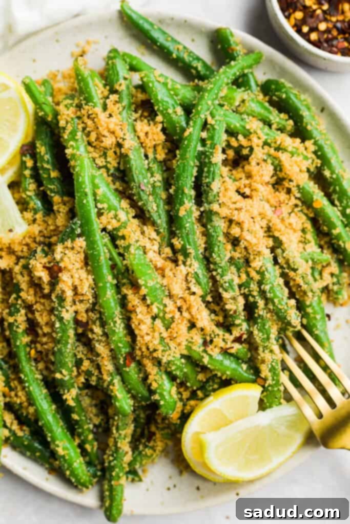 Plate of Italian green beans garnished with a lemon wedge and a sprinkle of red pepper flakes.