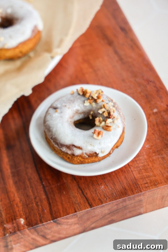 A pumpkin donut with glaze and chopped pecans.
