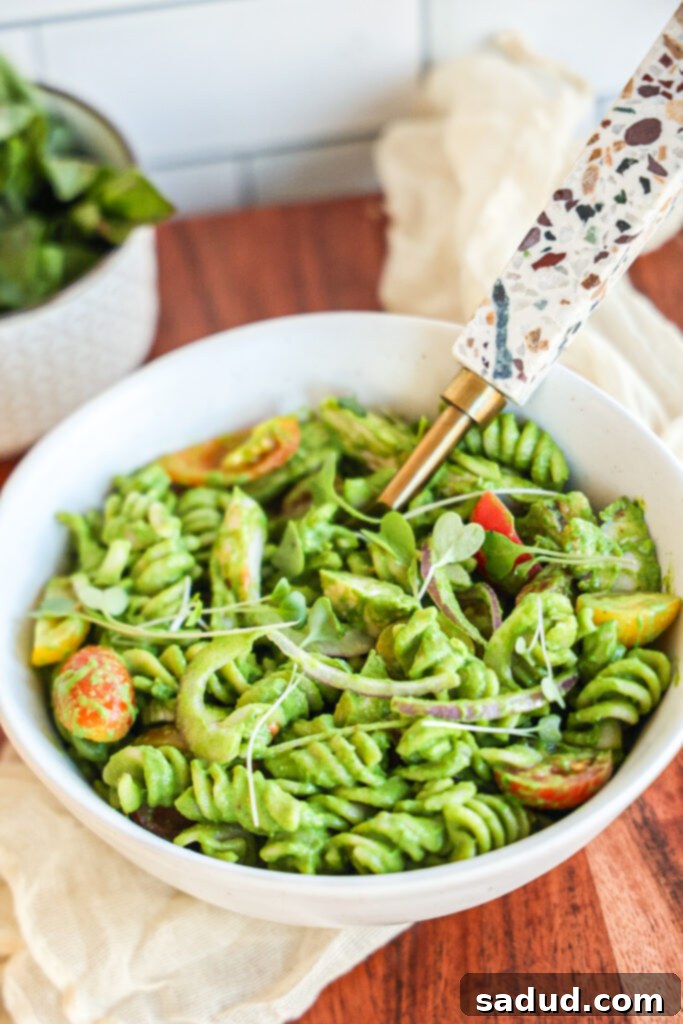 Close-up of a vibrant Green Goddess Pasta Salad in a bowl, showing pasta, cherry tomatoes, red onion, and creamy green dressing.