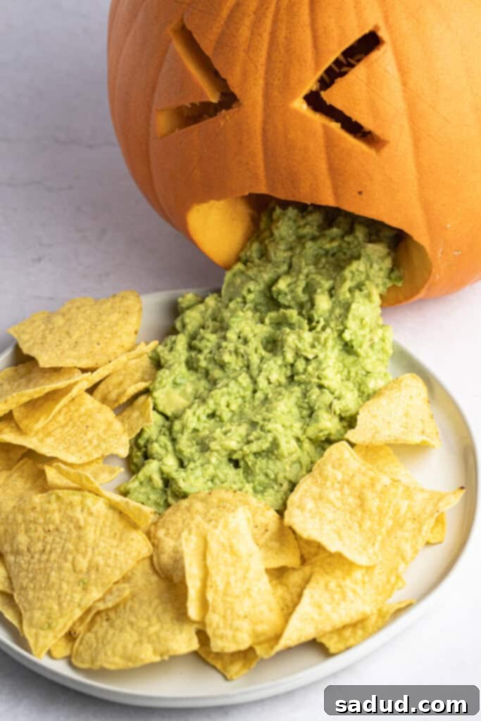Angled view of a puking pumpkin with guacamole creatively arranged on a plate surrounded by tortilla chips