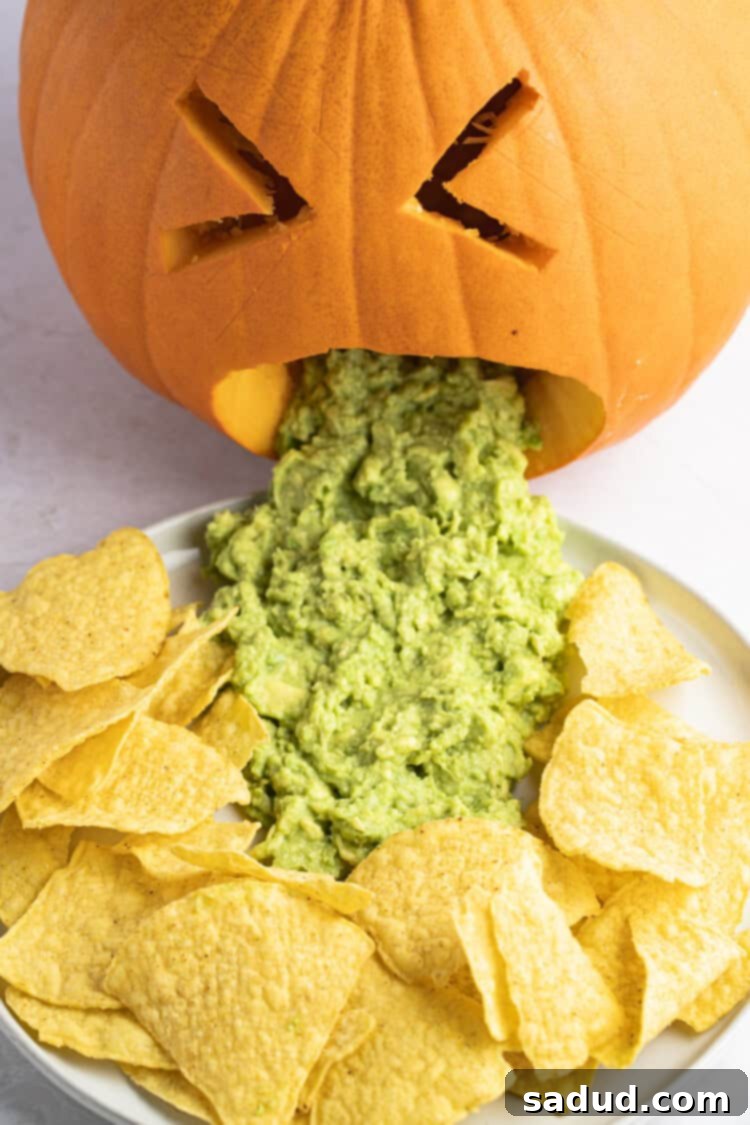 Close-up of a completed puking pumpkin, with guacamole flowing from its mouth onto a plate surrounded by tortilla chips