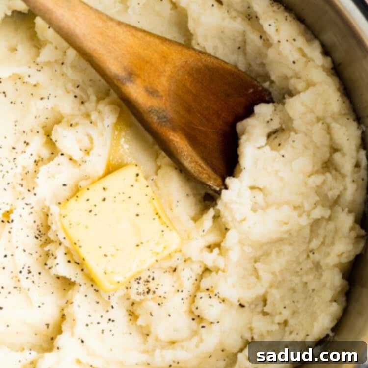 overhead image of mashed potatoes in a pot with butter and a wooden spoon