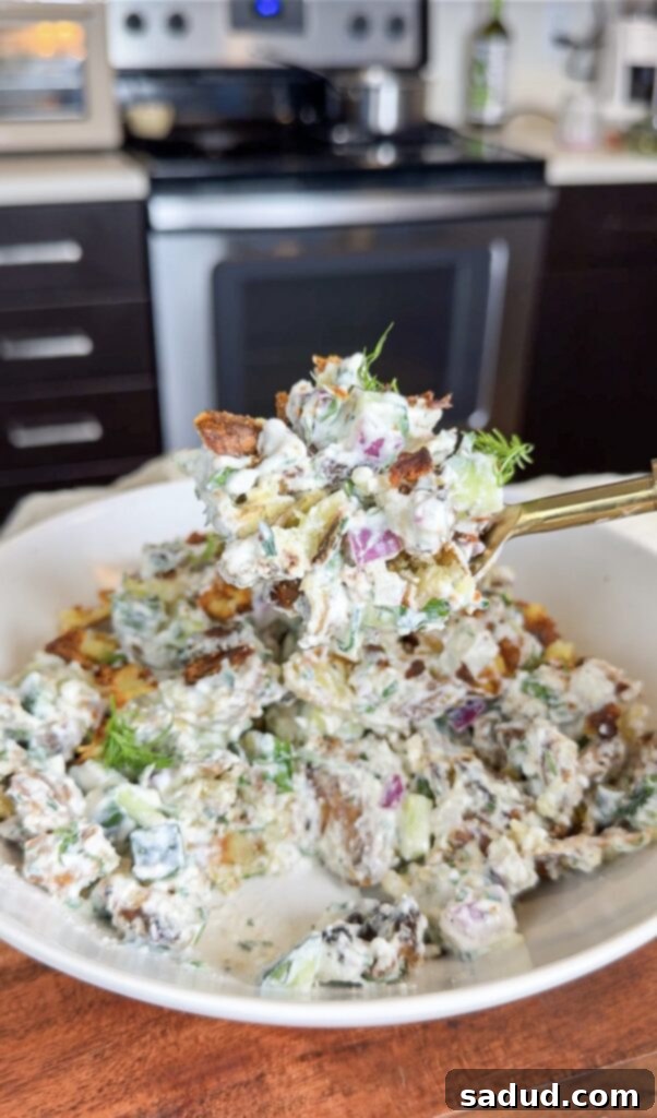 Crispy Smashed Potato Salad in a white bowl, with fresh herbs and lemon wedges.