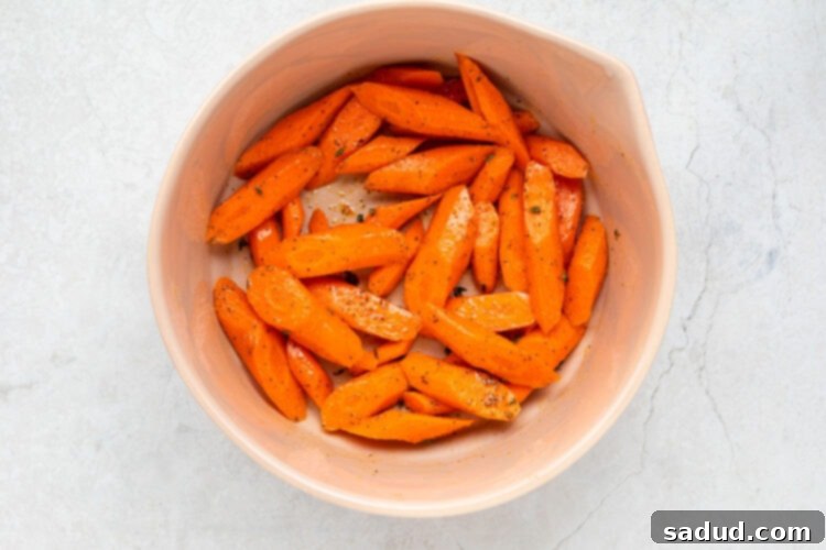 Sliced carrots in a large bowl, coated with seasoning.