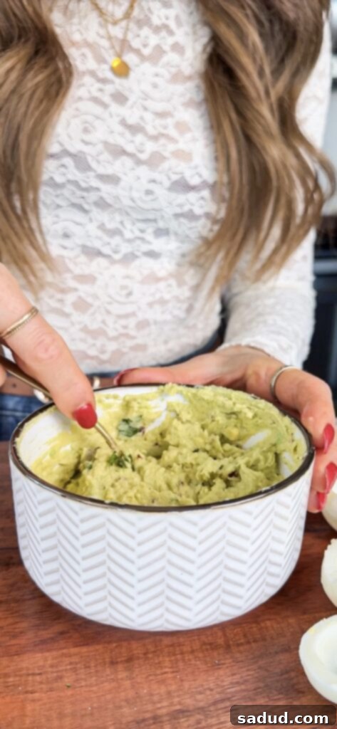 Creamy avocado filling being piped into egg white halves.