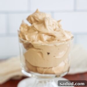 A close-up of a glass of iced Dalgona whipped honey coffee, with a rich, frothy topping over milk, garnished with a sprinkle of cinnamon, and a separate small bowl of the whipped coffee mixture.