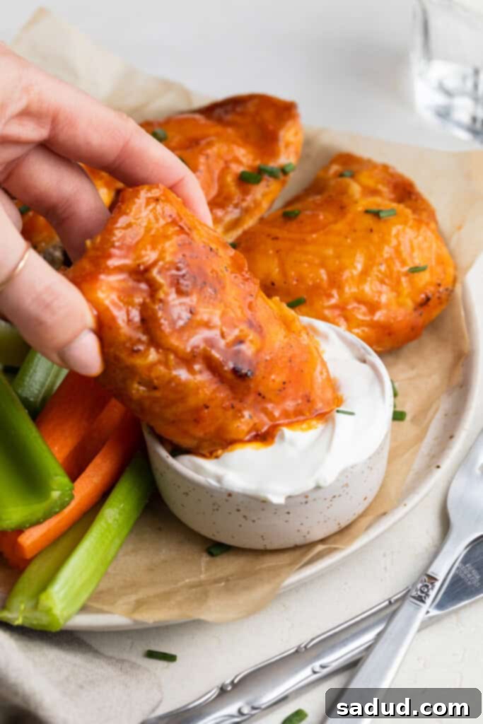 buffalo chicken thighs being dipped into a creamy sauce like sour cream or ranch