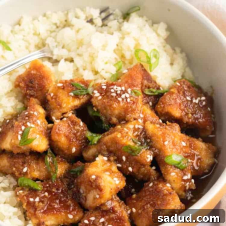 Keto orange chicken with green onions and sesame seeds on a bed of cauliflower rice