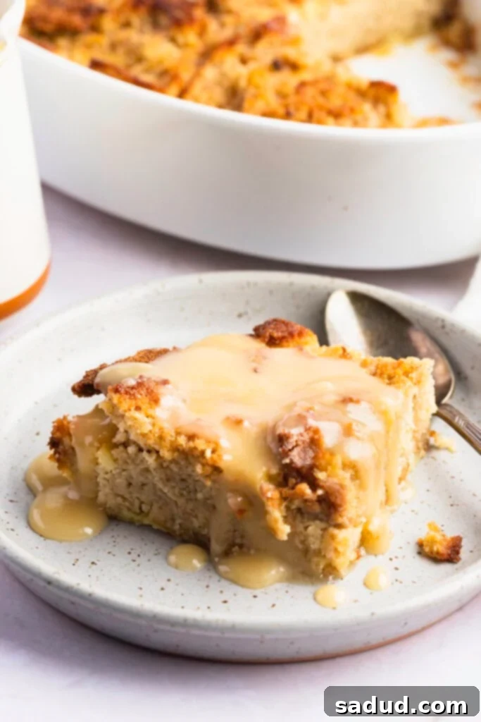A serving of keto bread pudding on a plate with a casserole dish in the background, showing its rich, golden-brown texture.