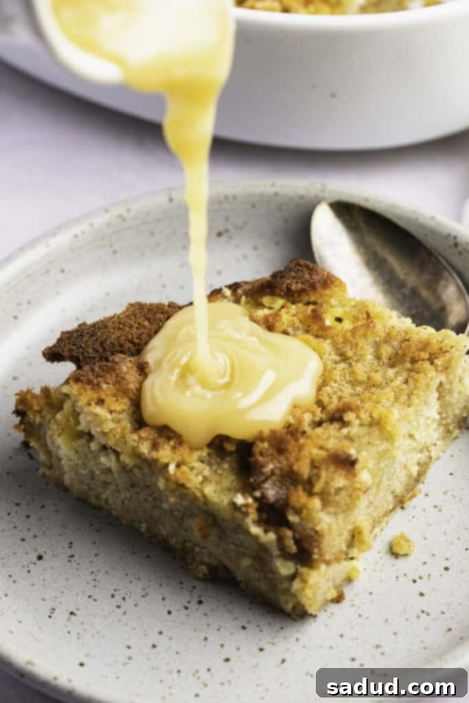 Vanilla sauce being poured over a square of golden keto bread pudding on a white plate, highlighting its rich topping.