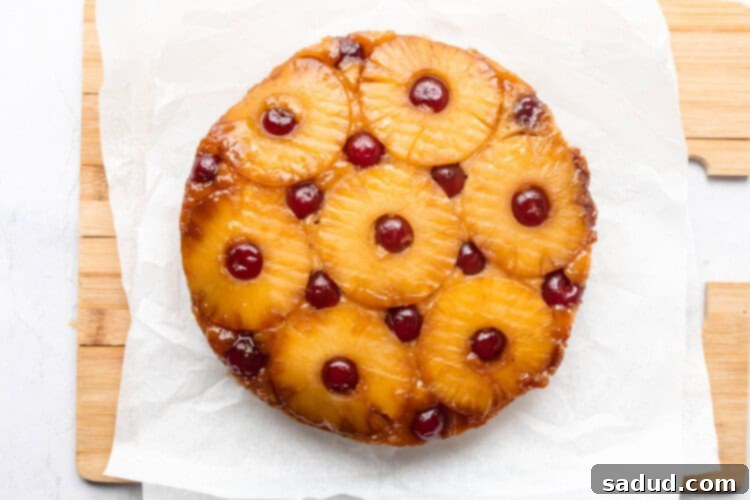 Round pineapple upside-down cake on parchment paper sitting on cutting board.