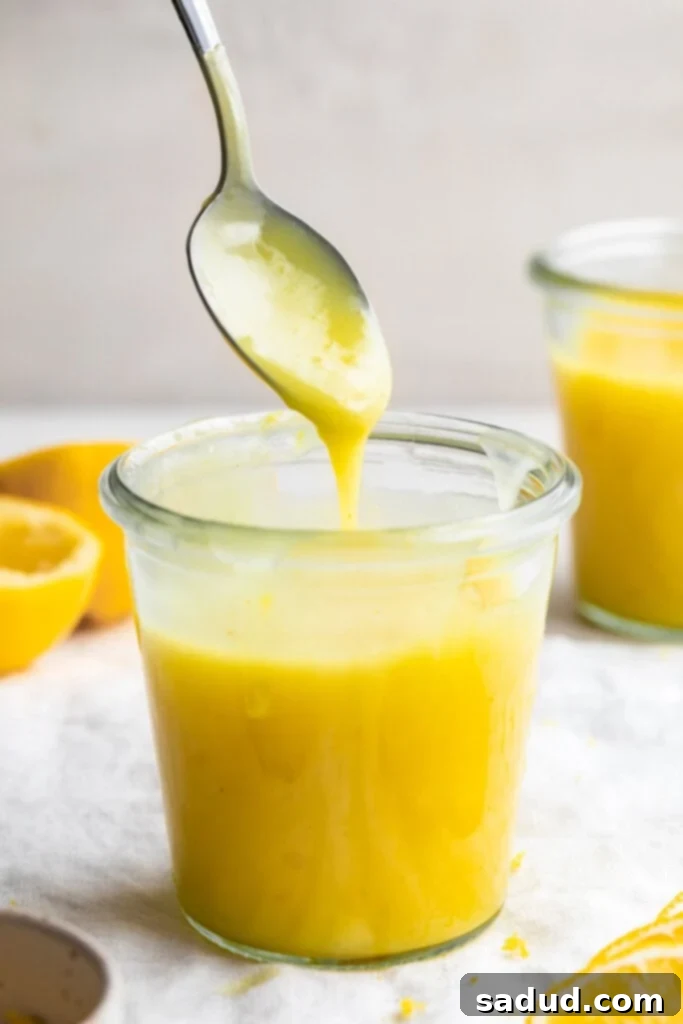 Vegan lemon curd in a glass jar with a spoon pouring more lemon curd into the jar.