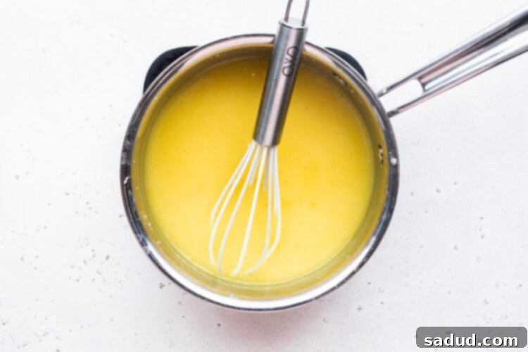 Overhead view of a small saucepan and whisk with bright yellow vegan lemon curd.