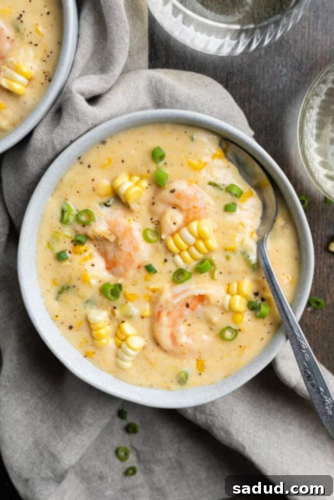 A beautifully presented bowl of creamy shrimp and corn soup, garnished, on a neutral cloth napkin, viewed from above, highlighting its rich texture and vibrant colors.
