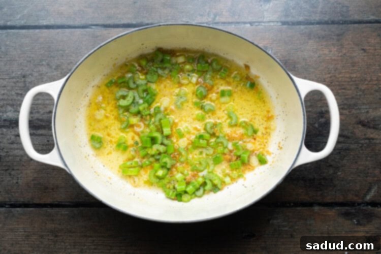 Overhead view of a large soup pot with melted butter, chopped celery, and white parts of green onions sautéing, forming the aromatic base for the soup.
