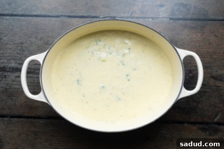 Overhead view of a large soup pot containing sautéed vegetables, flour, and slowly added milk and heavy cream for the creamy base of the shrimp and corn soup.
