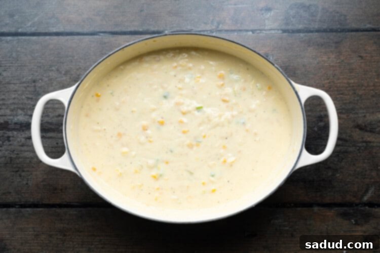 Overhead view of a large soup pot with cream-style corn and whole corn kernels added to the thickening creamy shrimp and corn soup base.