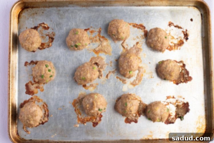 Overhead view of fully-cooked Asian turkey meatballs on a lightly greased baking sheet.