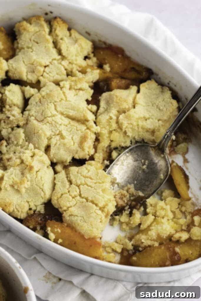 Overhead view of an angled casserole dish holding keto peach cobbler with a large silver spoon.