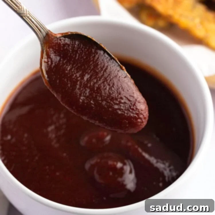 Vegan BBQ sauce in a small white bowl, with a spoon lifting a spoonful of sauce out of the bowl.