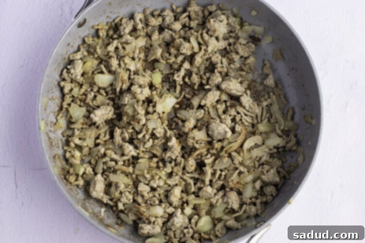 Overhead photo of ground turkey crumbled in large skillet, on a white background.