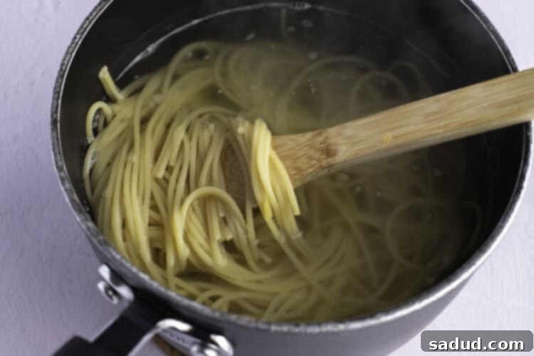 Cooked spaghetti noodles in a large silver pot, with a spoonful of noodles being held up with a wooden spoon.